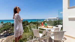 Un balcon avec une table et des chaises, offrant une vue sur la côte, avec des bâtiments et de la végétation.