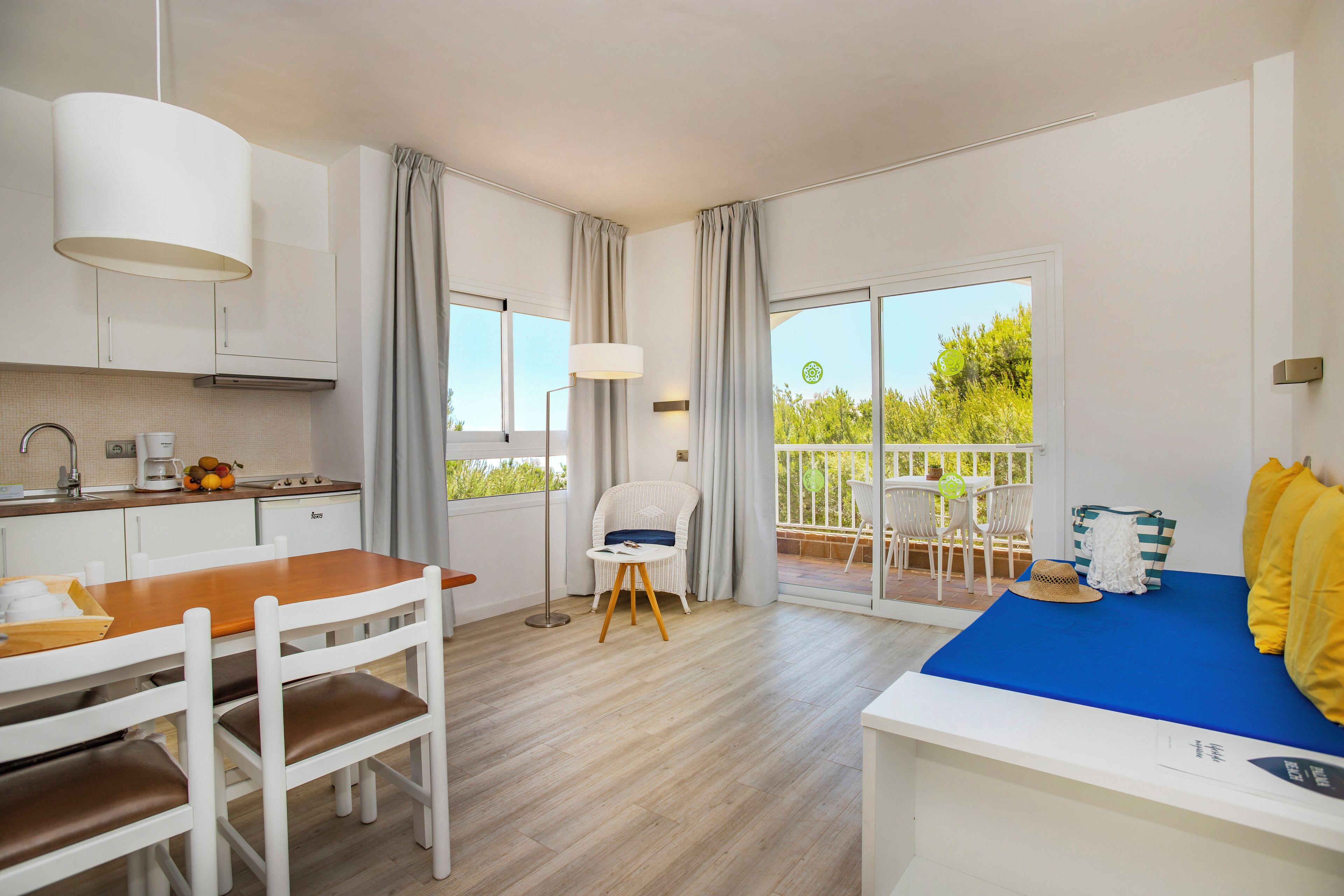 Una cocina moderna con armarios blancos, una mesa de comedor de madera y una cama azul con almohadas amarillas.