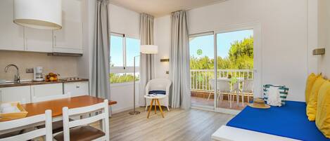 A modern kitchen with white cabinets, a wooden dining table, and a blue bed with yellow pillows.
