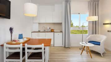 A modern kitchen with white cabinets, a dining table with chairs, a small refrigerator, and a window with curtains.
