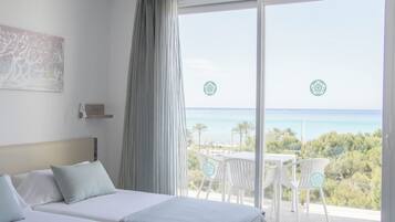 A hotel room with a bed, a view of the sea, and a balcony with chairs.