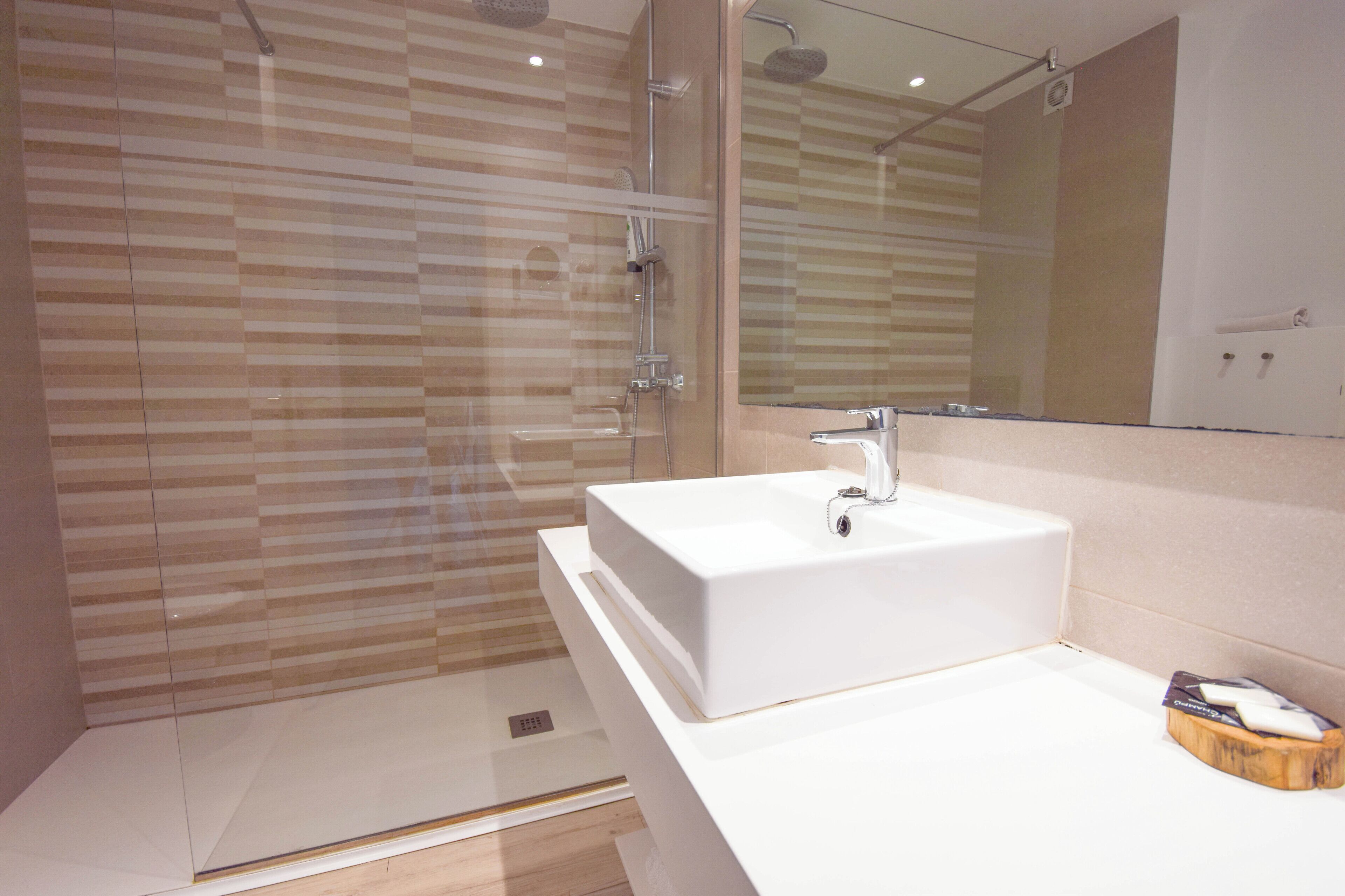 A modern bathroom with a glass shower enclosure, a white sink, and a large mirror.