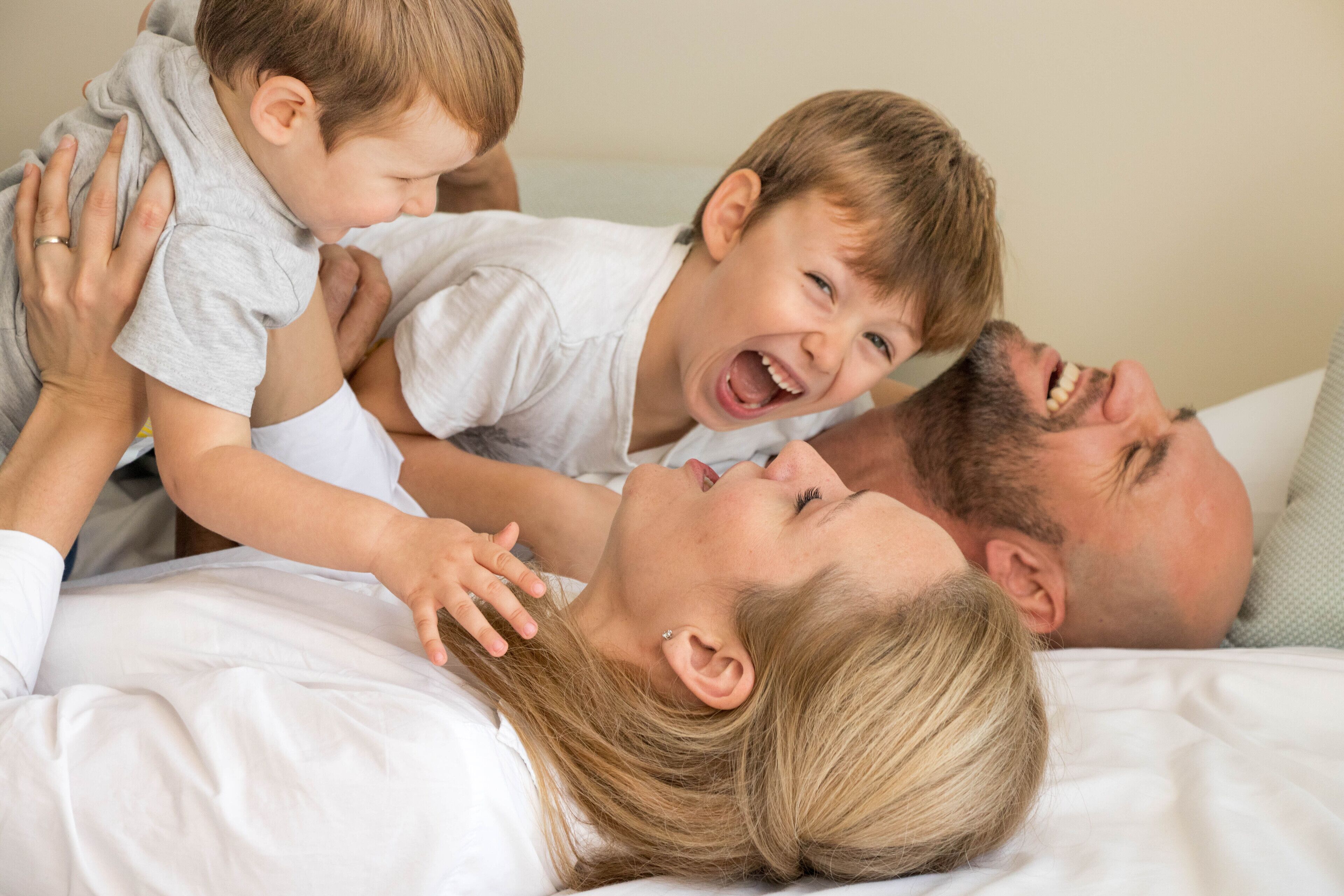 Eine Familie mit drei Personen in einem Schlafzimmer mit Bett und Kissen.