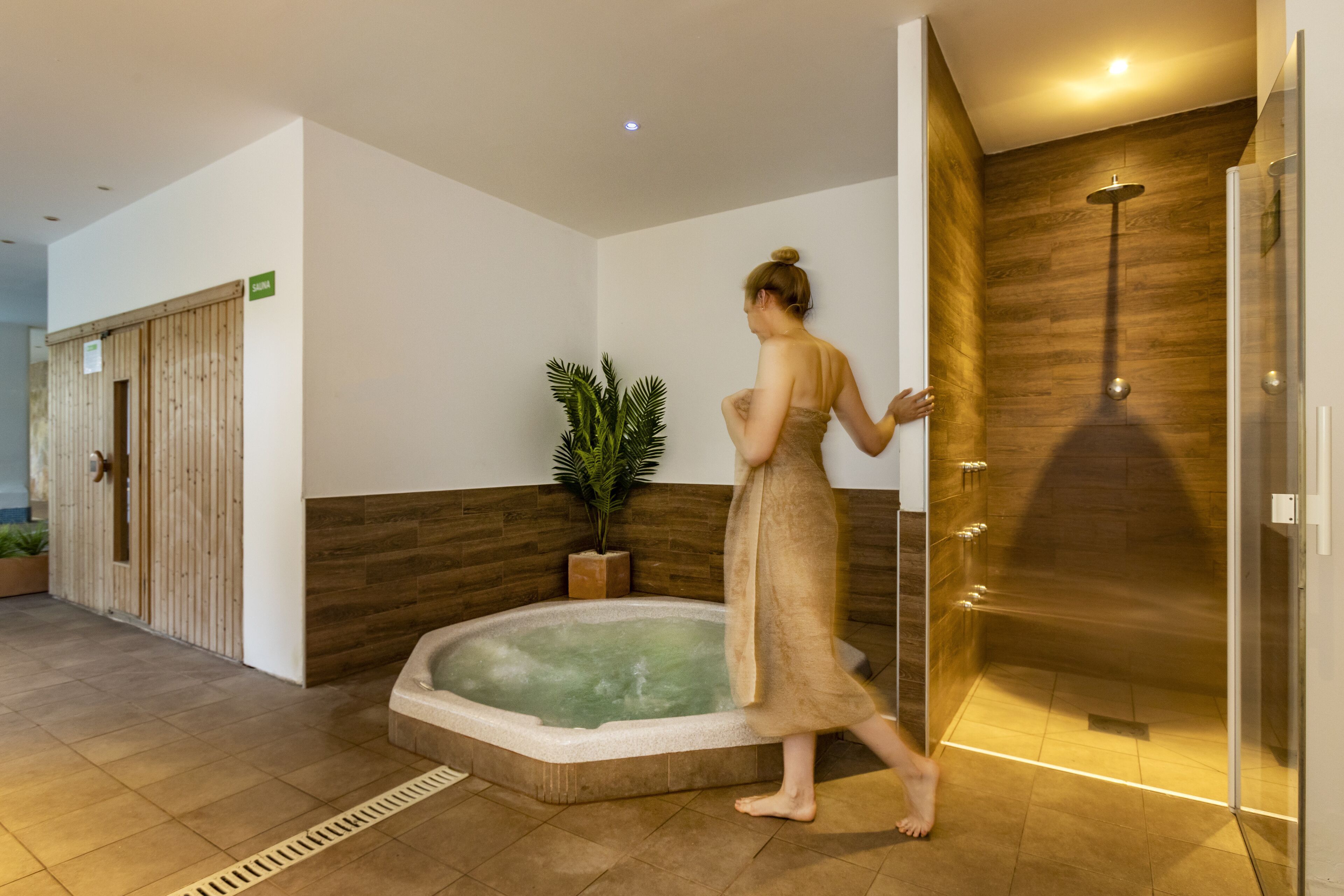 A spa area with a hot tub, a wooden wall, and a glass shower enclosure.