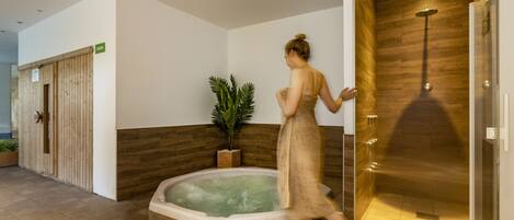 A spa area with a hot tub, a wooden wall, and a glass shower enclosure.