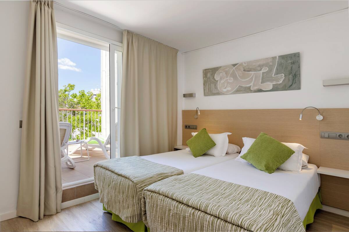 Habitación de hotel con dos camas, un balcón y vista a zonas verdes.