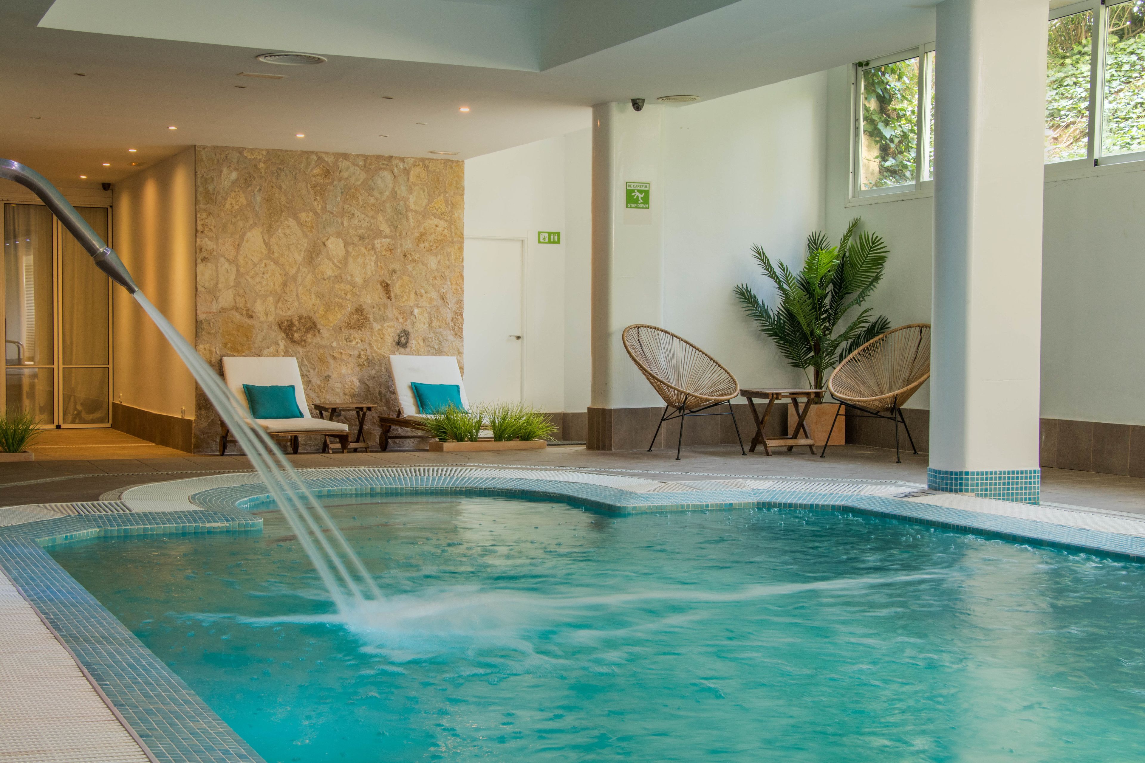 Une piscine agrémentée d’un élément décoratif aquatique, entourée de chaises longues et d’un mur en pierre.