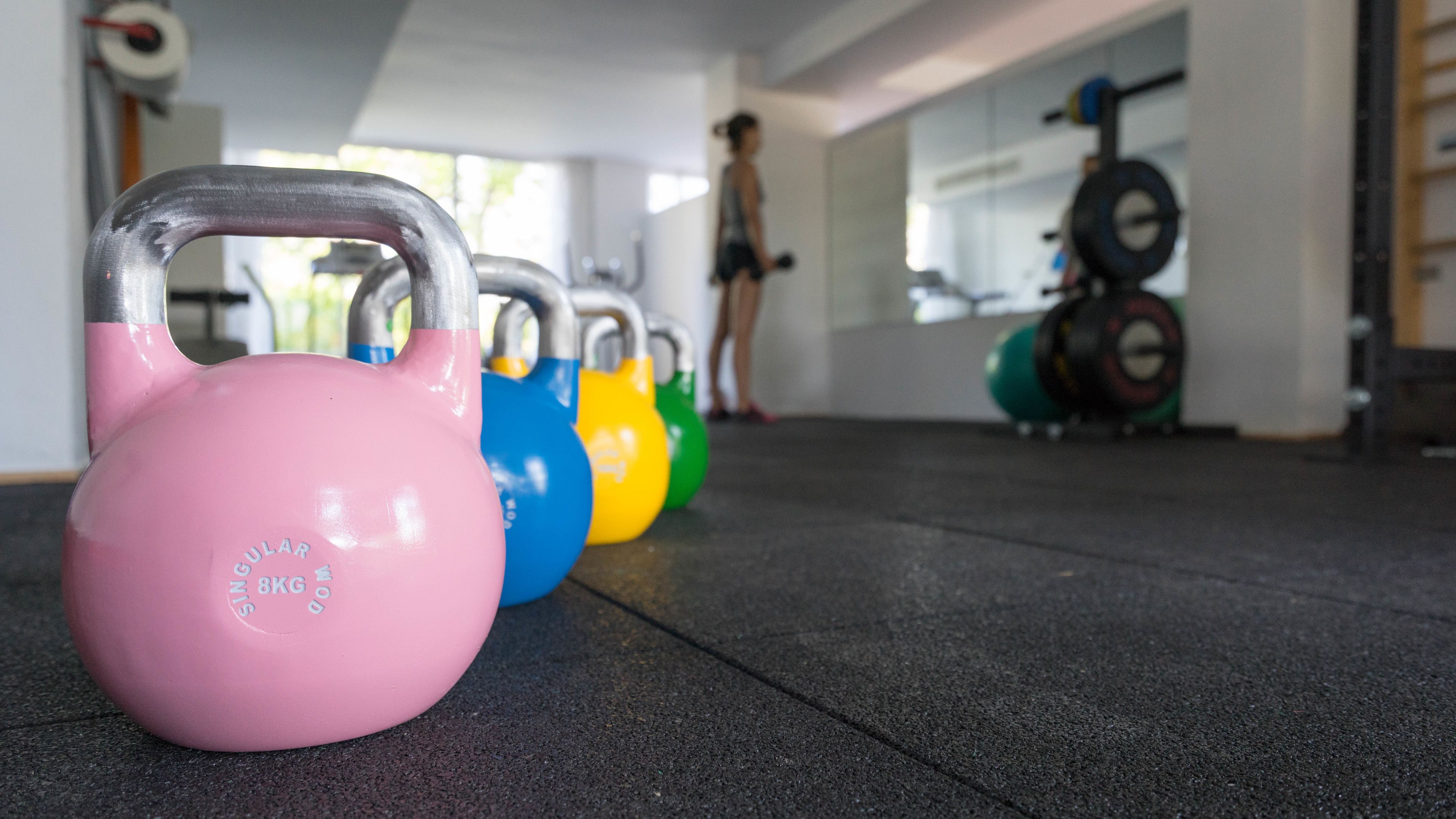 A row of kettlebells in various colors lined up on a gym floor.