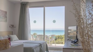 Une chambre d’hôtel avec deux lits, un balcon donnant sur la mer et un bureau équipé d’un ordinateur et de documents.