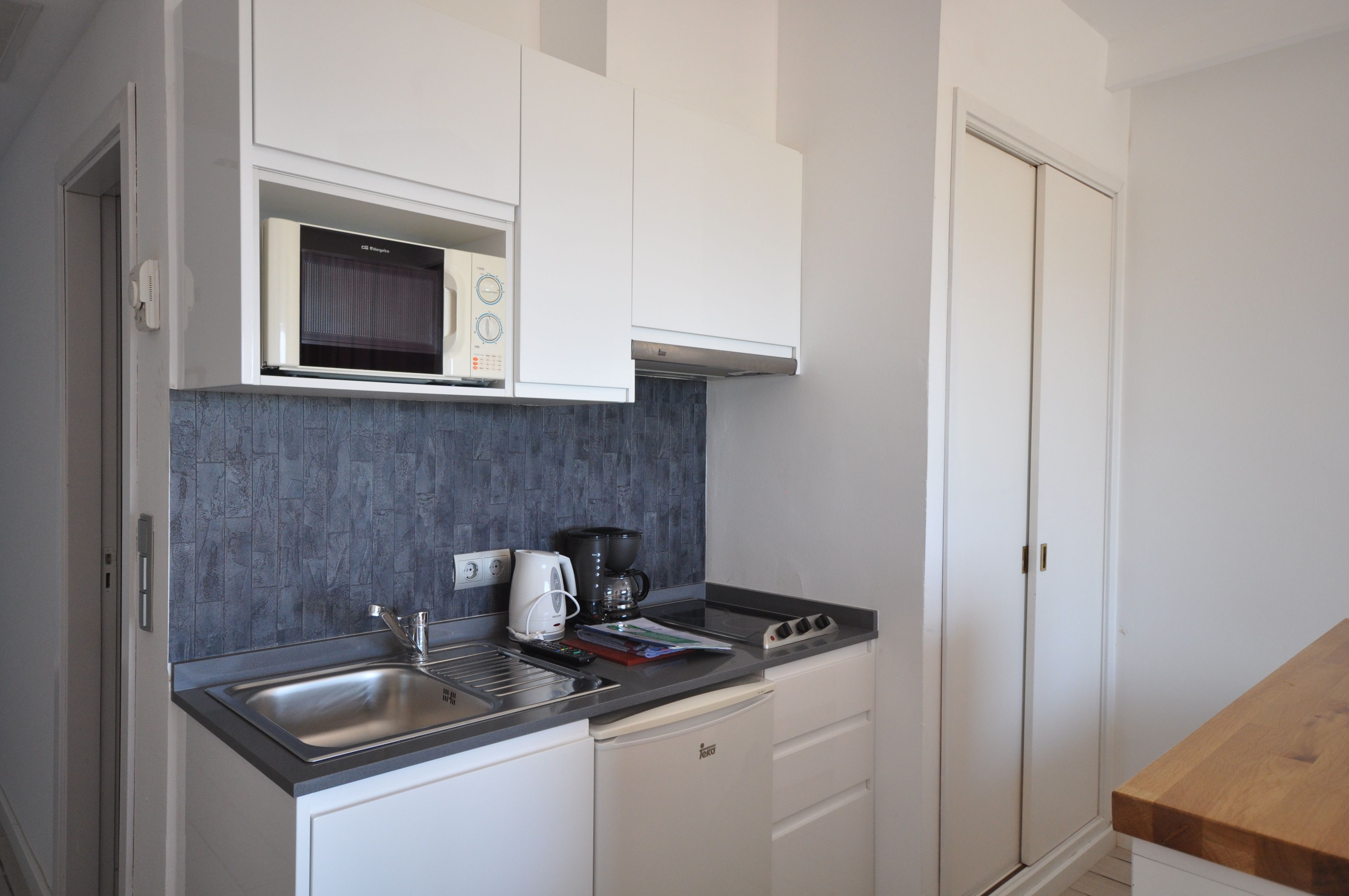 Una cocina compacta con armarios blancos, microondas, cafetera y tostadora.