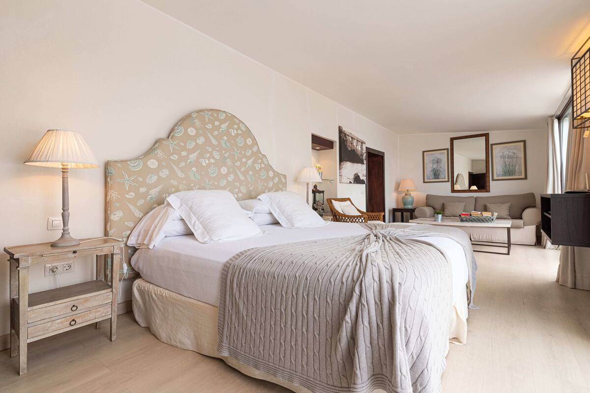 A bedroom with a bed, bedside table, lamp, and a sofa.