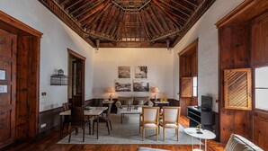 A spacious living area with a high wooden ceiling, a sofa, a dining table with chairs, and a television. - Isla Baja Suites (Garachico)