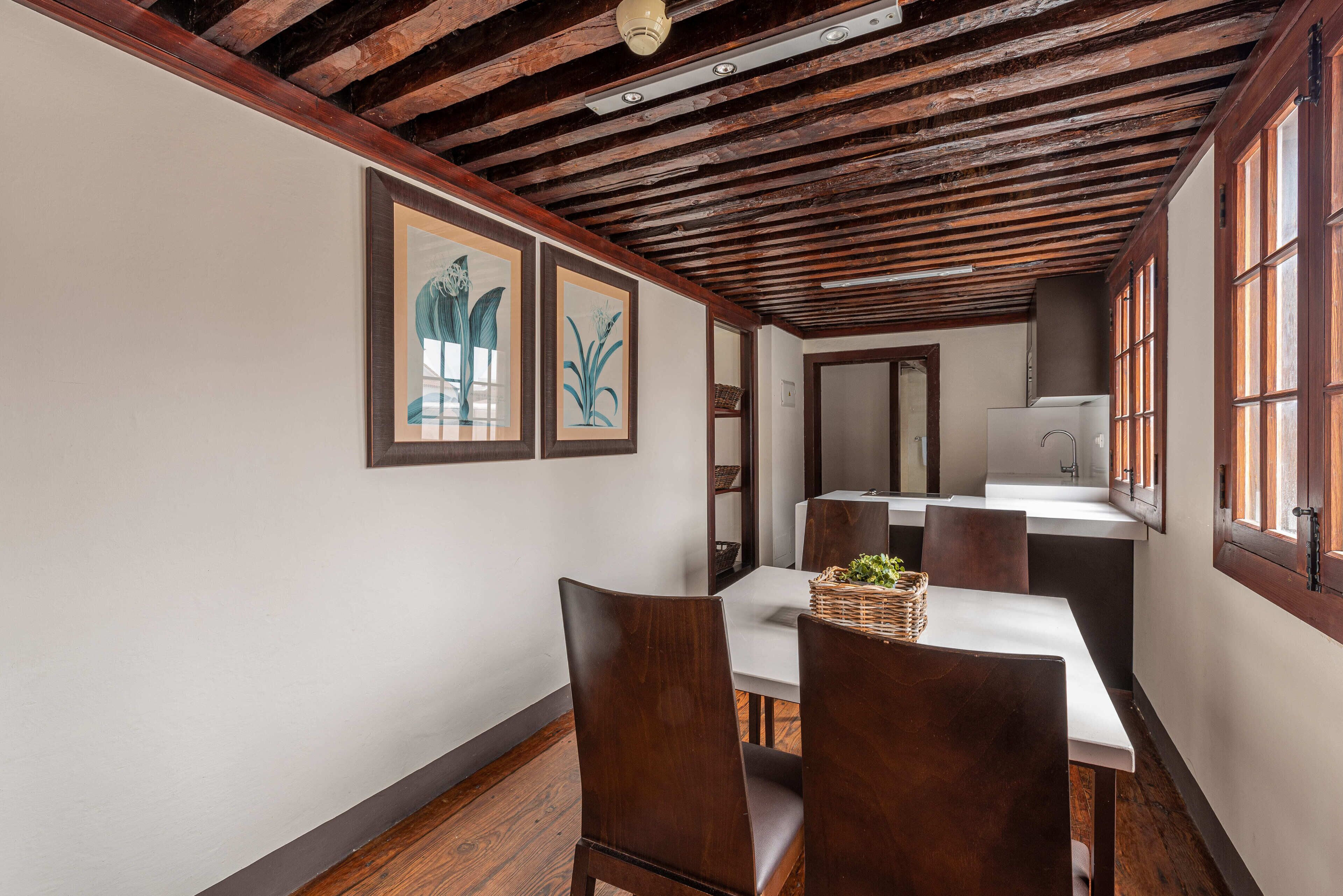 Un'area pranzo con sedie di legno, un tavolo bianco e opere d'arte incorniciate appese al muro.