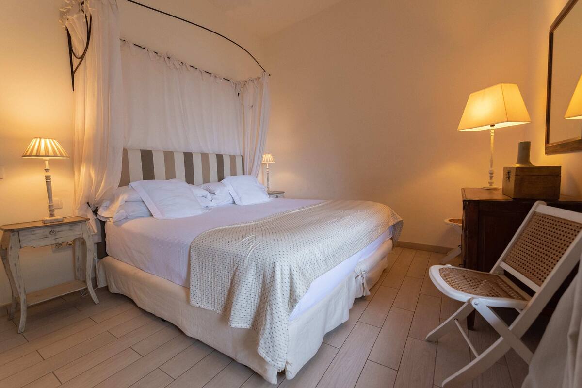 A neatly arranged bedroom with a large bed, two bedside tables with lamps, a chair, and a wooden dresser.