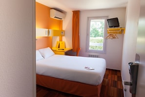 Une chambre d’hôtel avec un lit, un bureau, une chaise, une télévision et une fenêtre avec des rideaux.