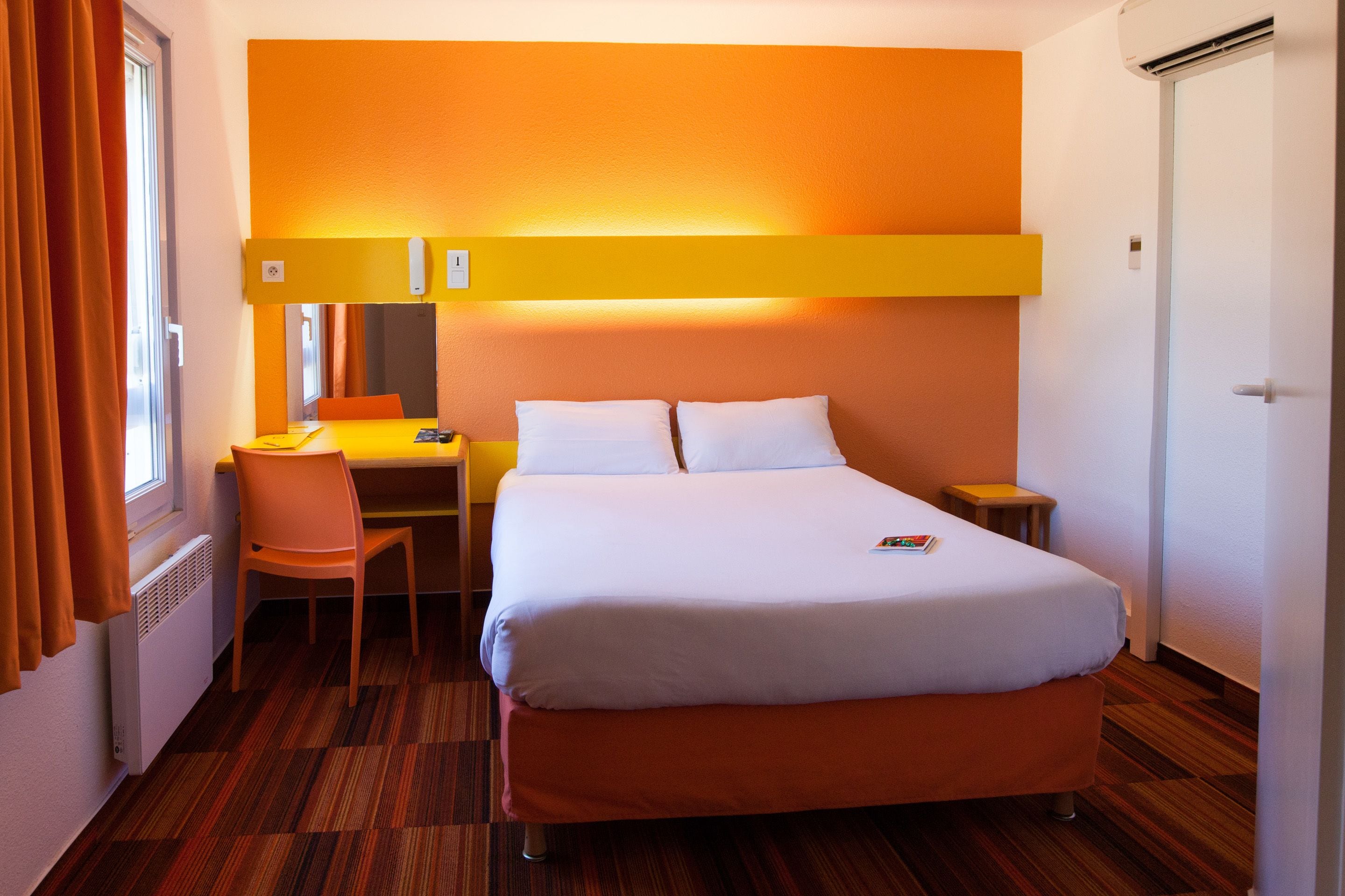 A hotel room with a bed, a desk, a chair, and a small table.