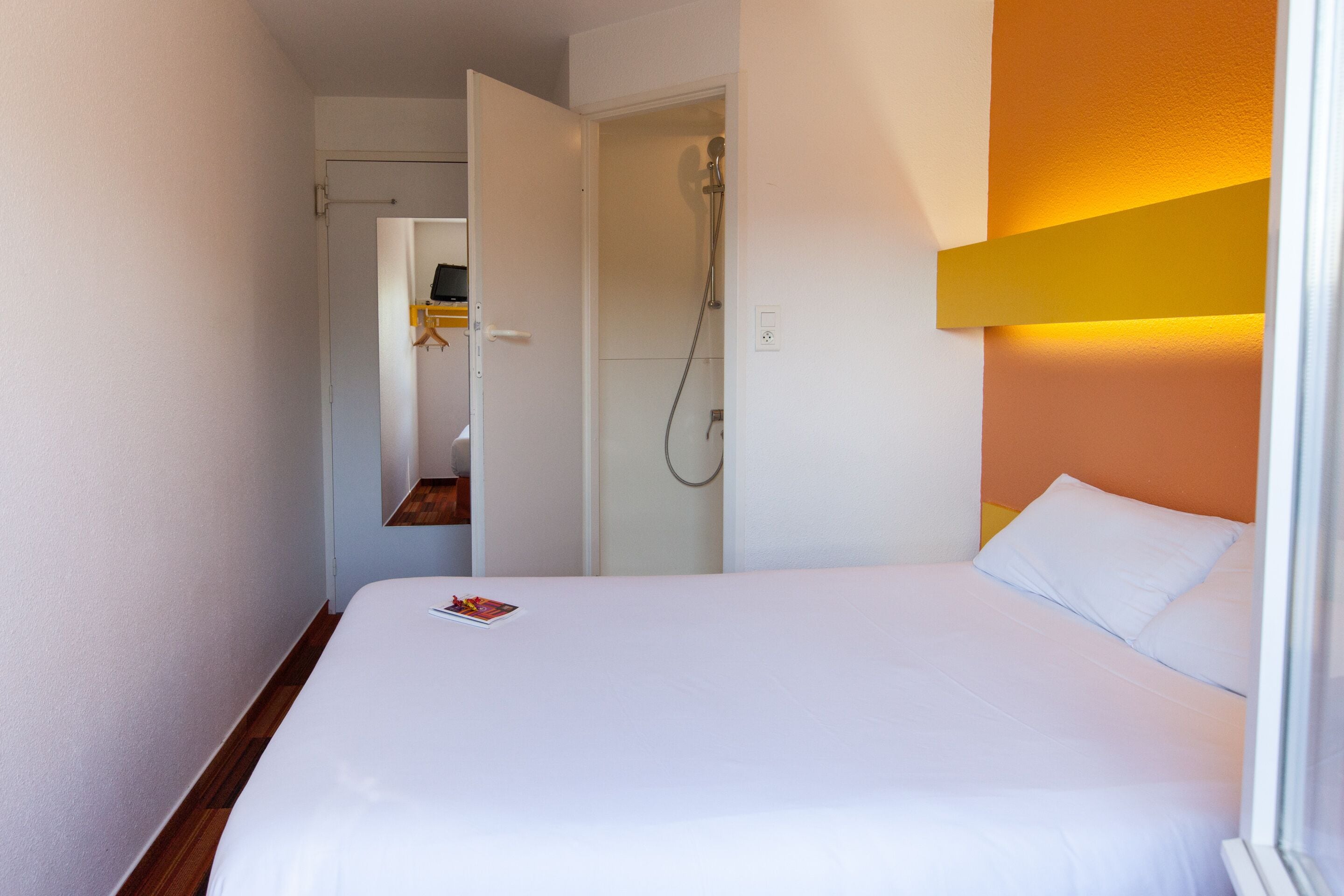 A hotel room with a bed, a shower, and a door leading to a hallway.