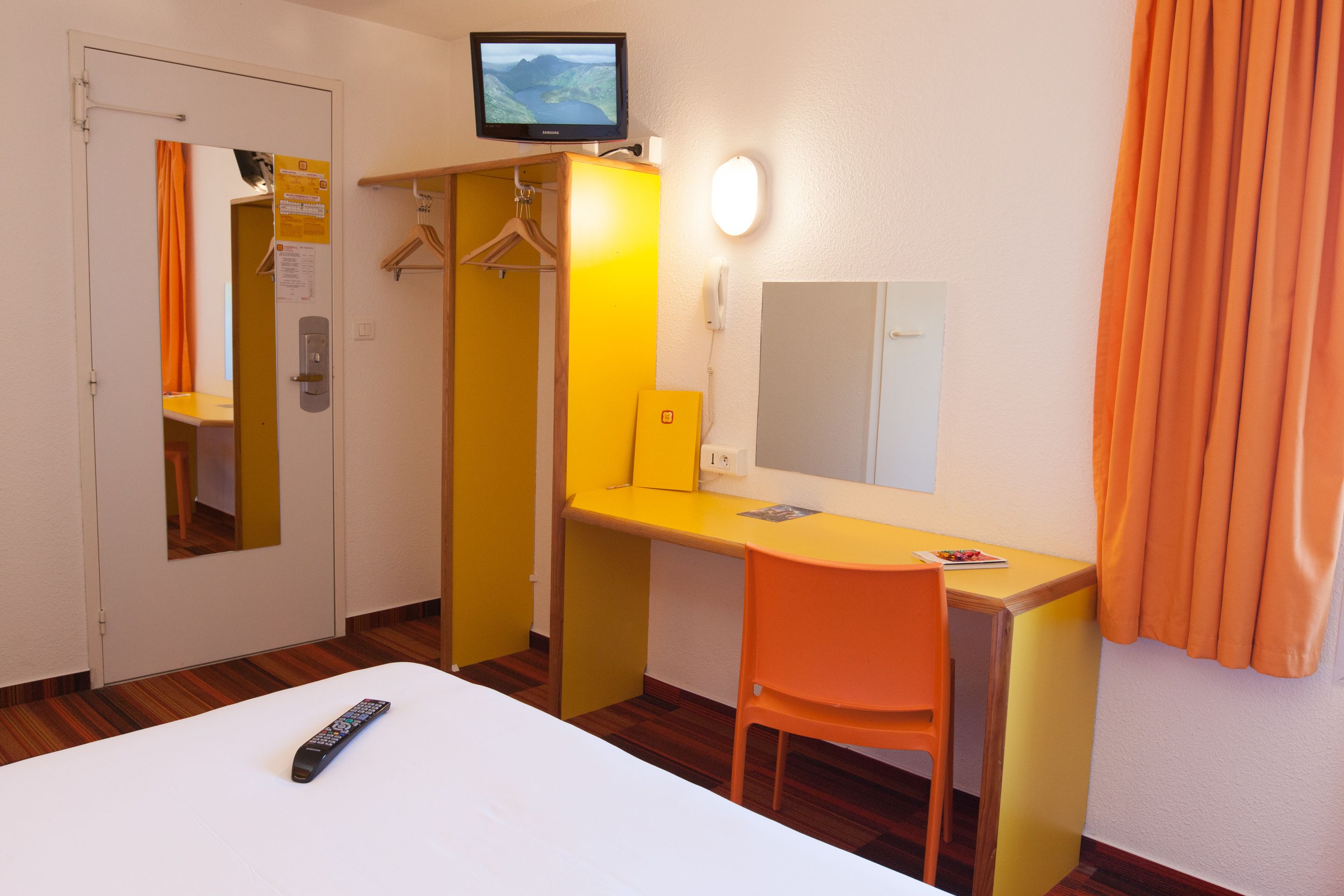 Hotellihuone, jossa on sänky, työpöytä, tuoli, televisio, peili ja puhelin.