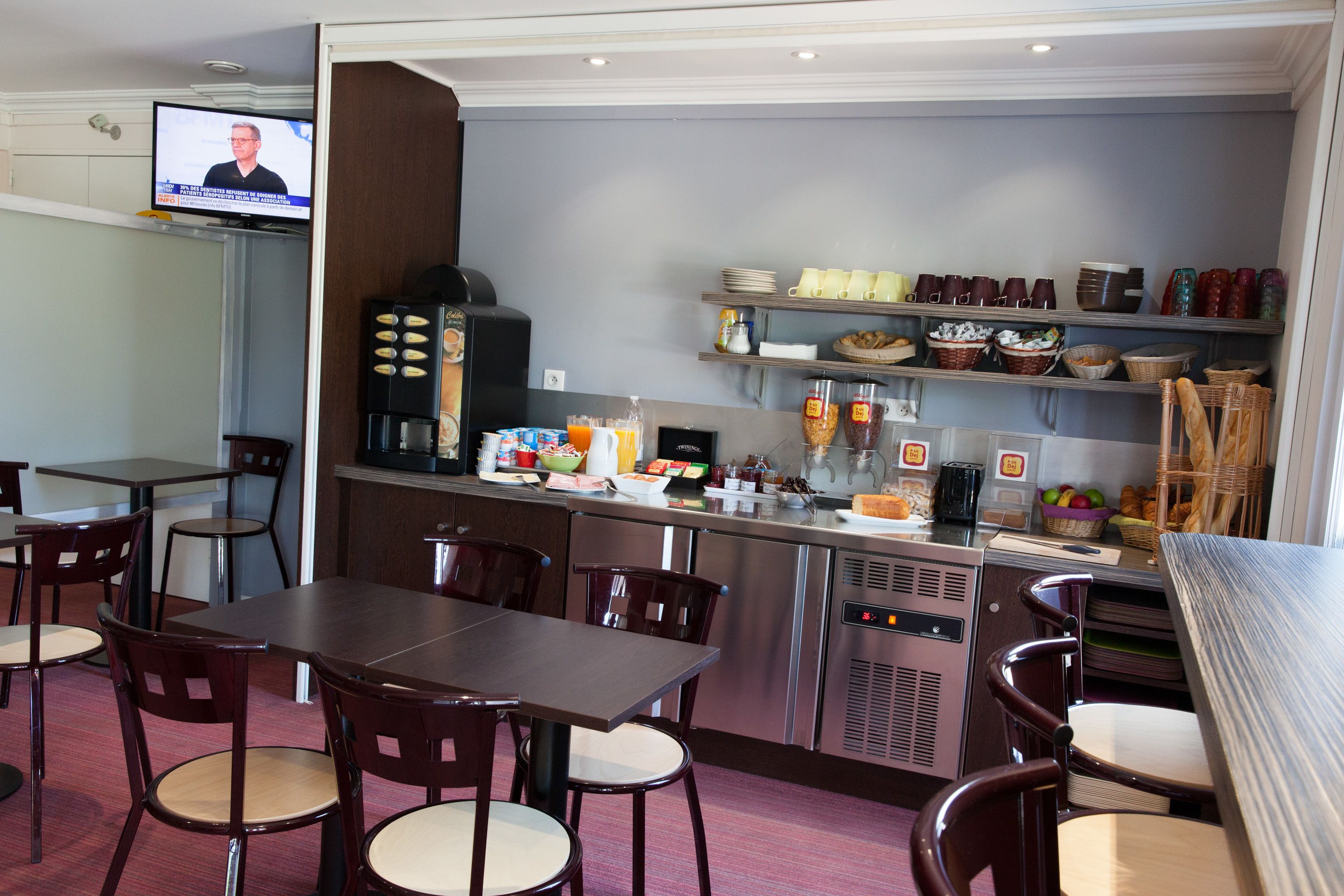 Un restaurante con una televisión mostrando un programa de noticias, una cafetera y varios alimentos en estantes.