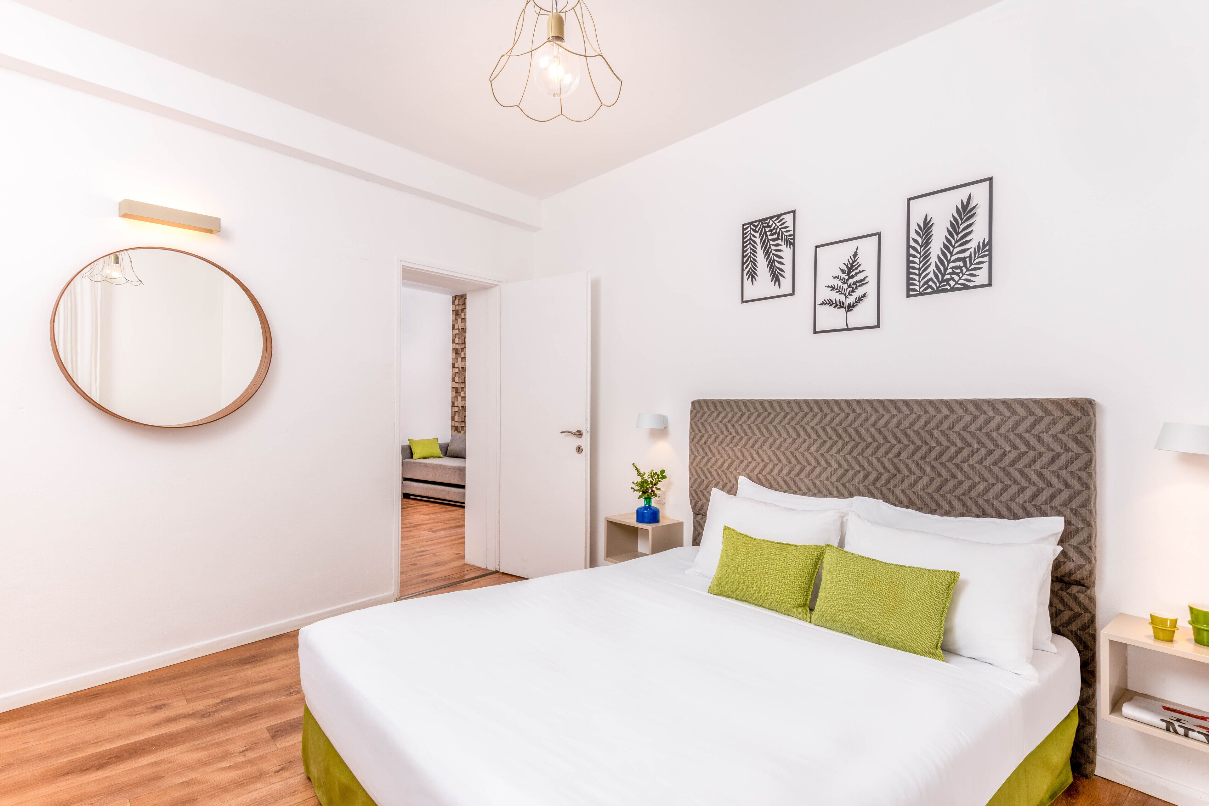 Una habitación de hotel moderna con una cama grande, un espejo redondo y tres obras de arte con motivos de hojas.