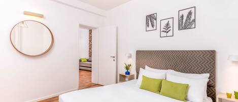 Una habitación de hotel moderna con una cama grande, un espejo redondo y tres obras de arte con motivos de hojas.