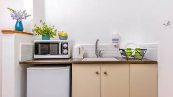 Cocina compacta equipada con microondas, tostadora y un refrigerador pequeño. Hay plantas en macetas y un lavamanos con dispensador de jabón.