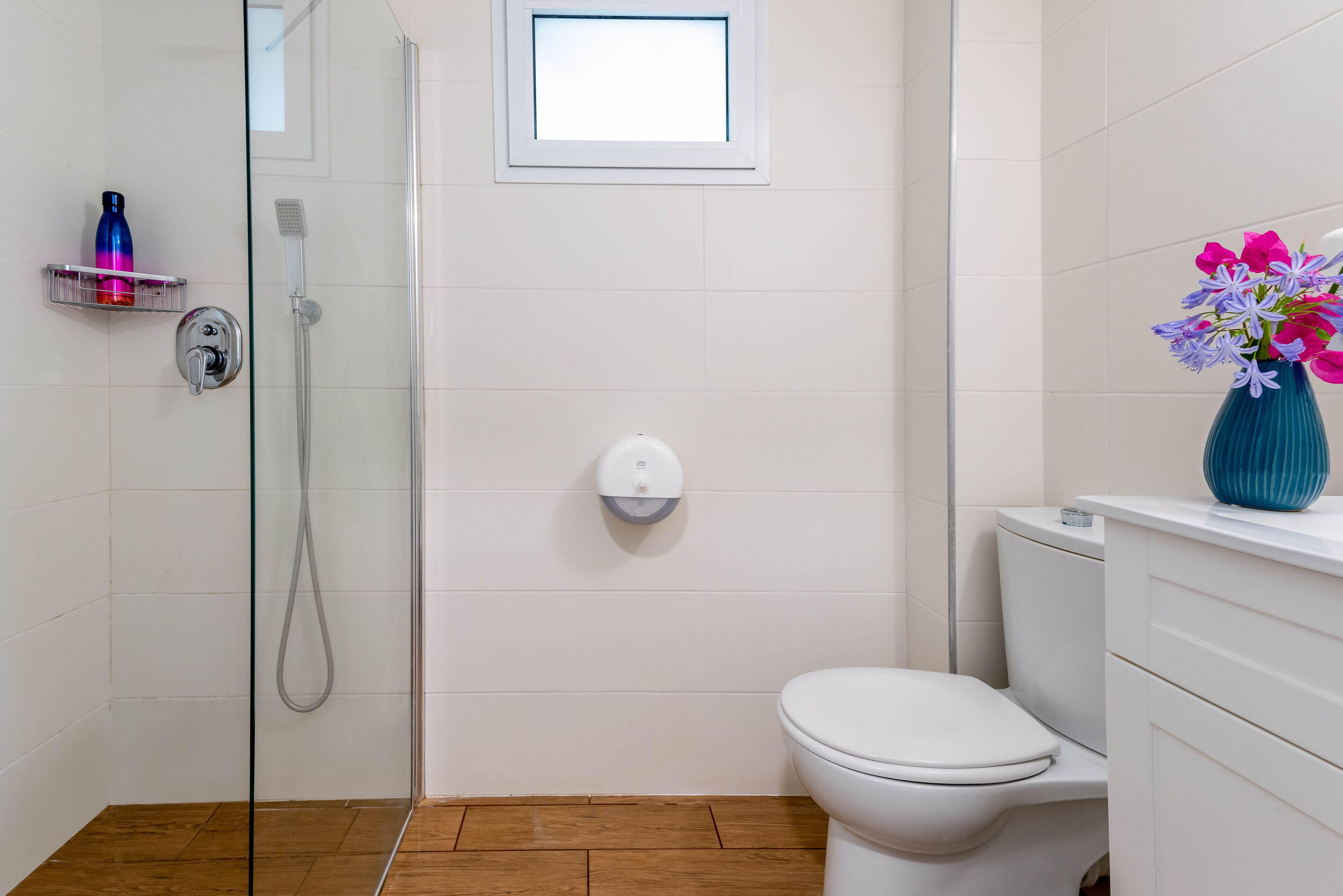 Une salle de bain moderne avec une douche à l’italienne en verre, des toilettes et une petite fenêtre située au-dessus des toilettes.