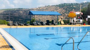 A swimming pool with clear blue water, surrounded by lounge chairs and a covered seating area. - Eilon TravelHotel (Mateh Asher)
