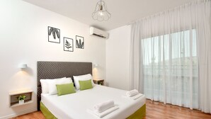 A neatly made bed with white and green bedding, a grey headboard, and two bedside tables with lamps. - Eilon TravelHotel (Mateh Asher)