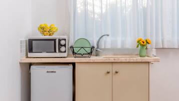 A compact kitchen with a microwave, a dish rack, a sink, and a refrigerator.