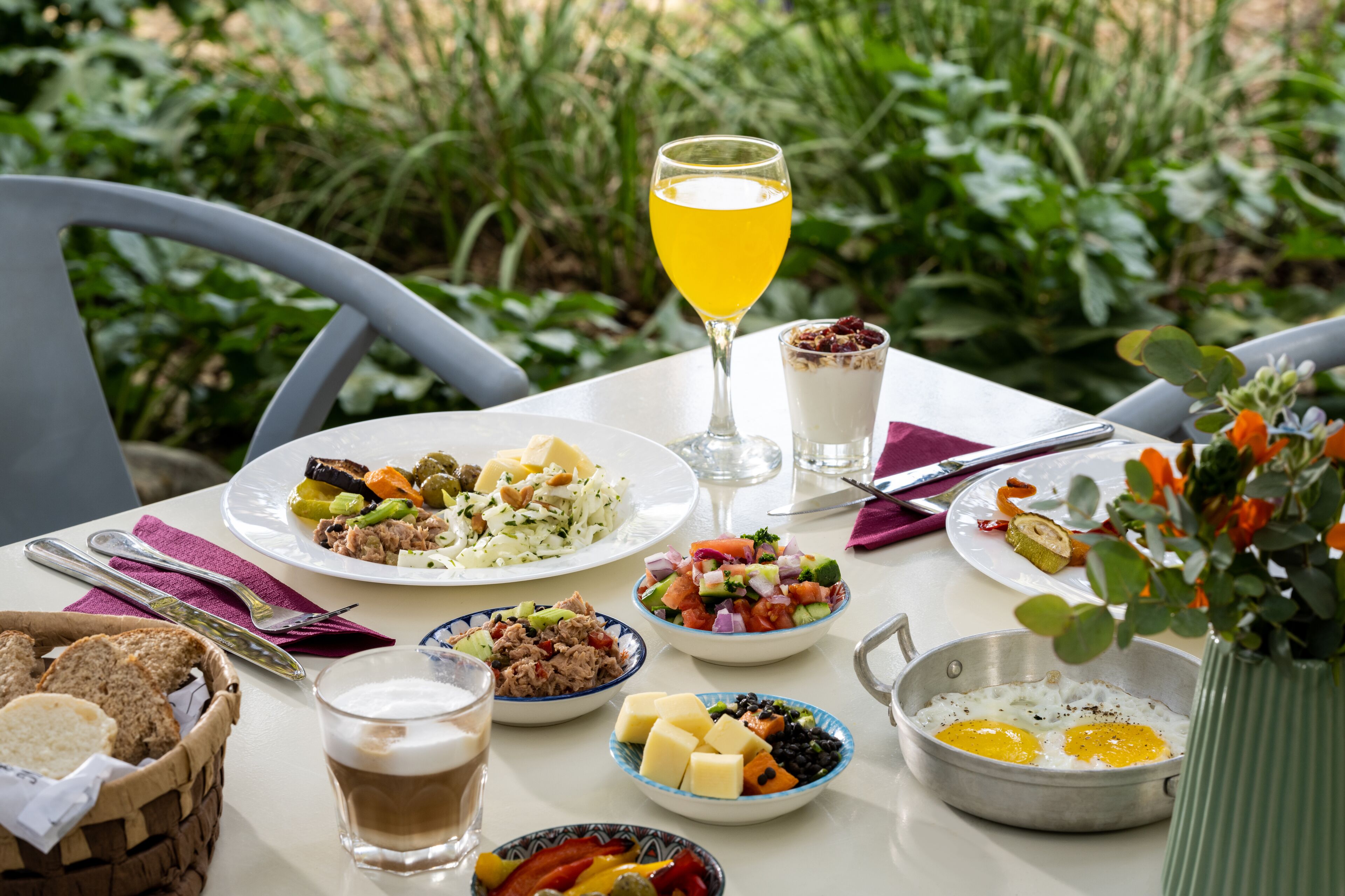 Una mesa servida con varios platos, un vaso de jugo y una pequeña planta.