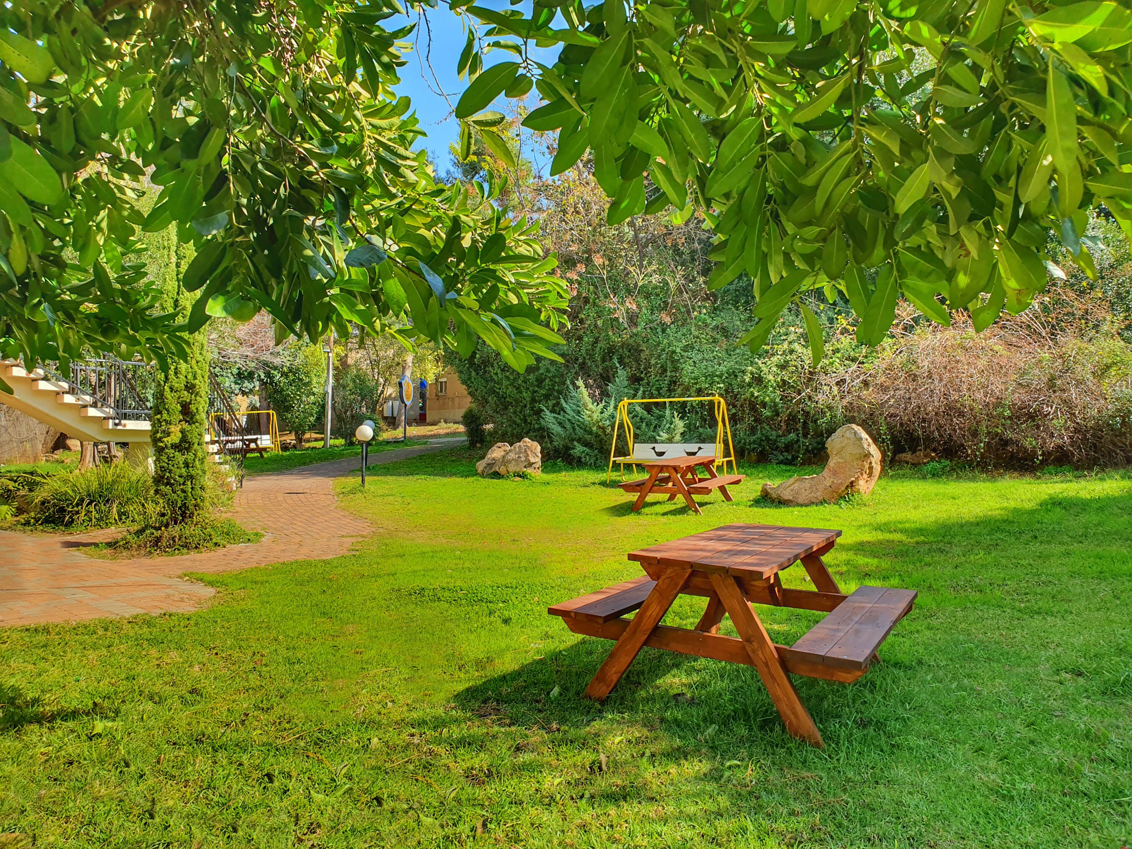 A picnic area with a wooden table and benches, surrounded by lush greenery and a swing set.