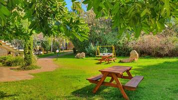 Un área de picnic con una mesa y bancos de madera, rodeada de abundante vegetación y un columpio.