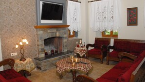 A living room with a fireplace, a television mounted above it, and a red sofa. - Filoxenia (Volos)
