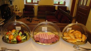A buffet table with three covered dishes: one with fruits, one with meats, and one with pastries. - Filoxenia (Volos)