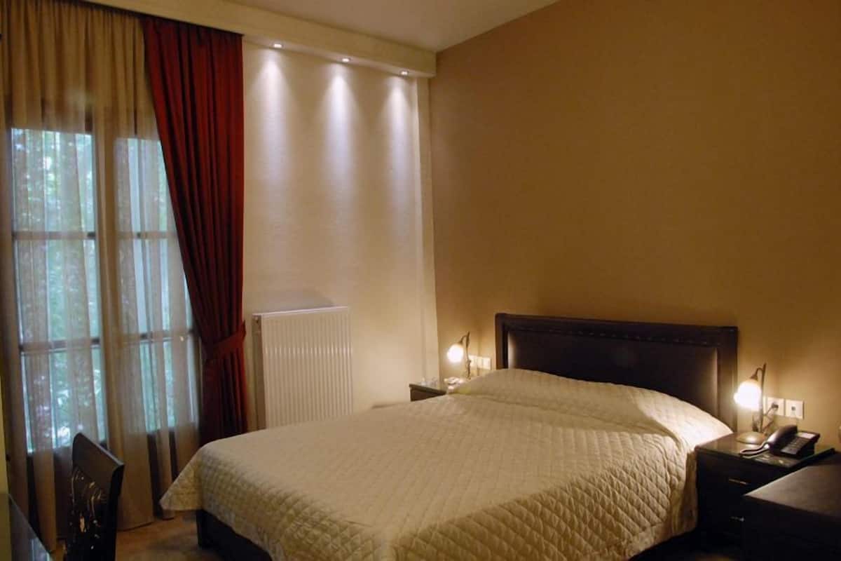 A hotel room with a large bed, a nightstand with a lamp, and a view of trees through the window.