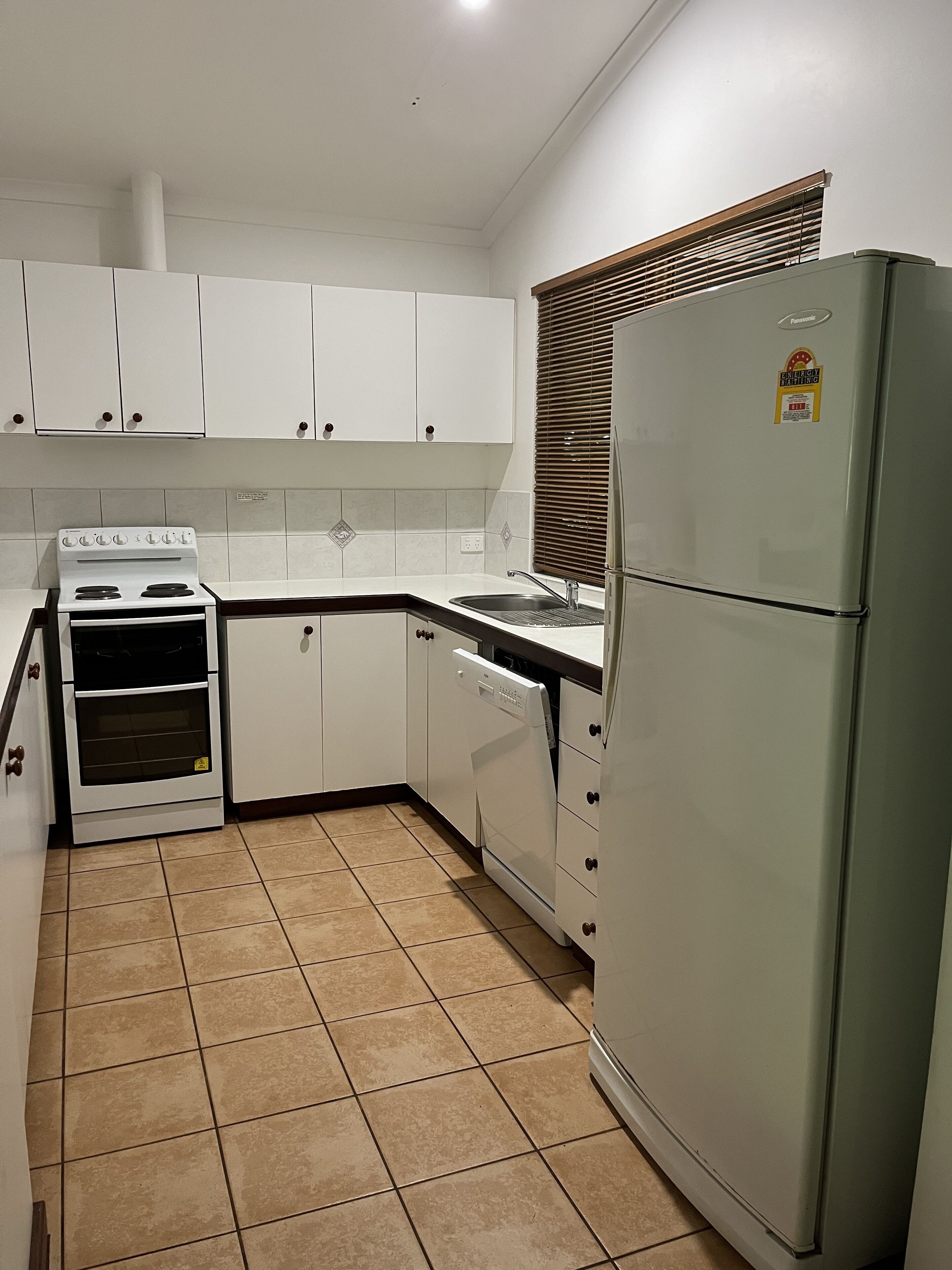 Eine kleine Küche mit weißen Schränken, einem Backofen, einem Geschirrspüler und einem Kühlschrank.