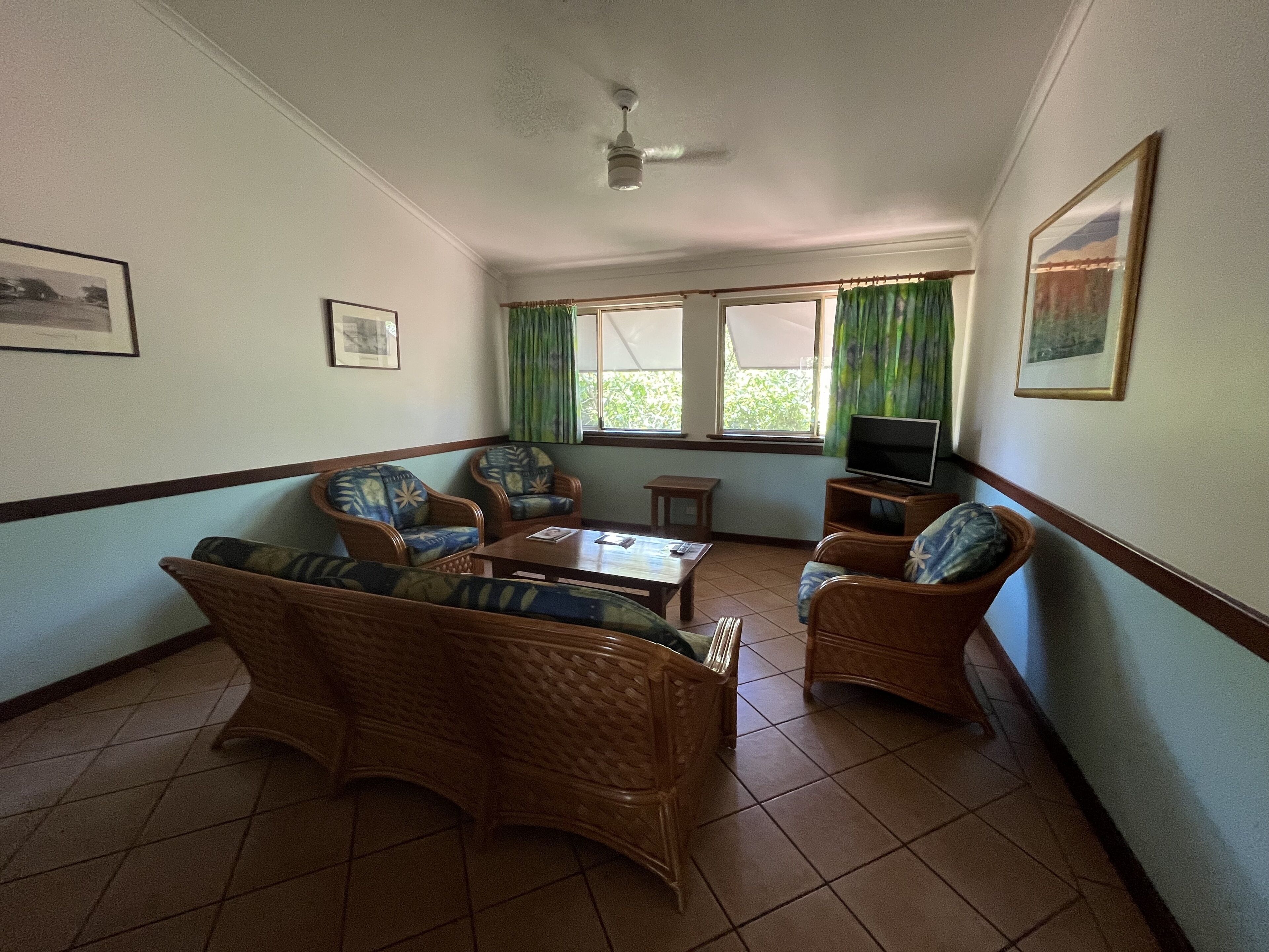 A living room with wicker furniture, a ceiling fan, and a television on a stand.