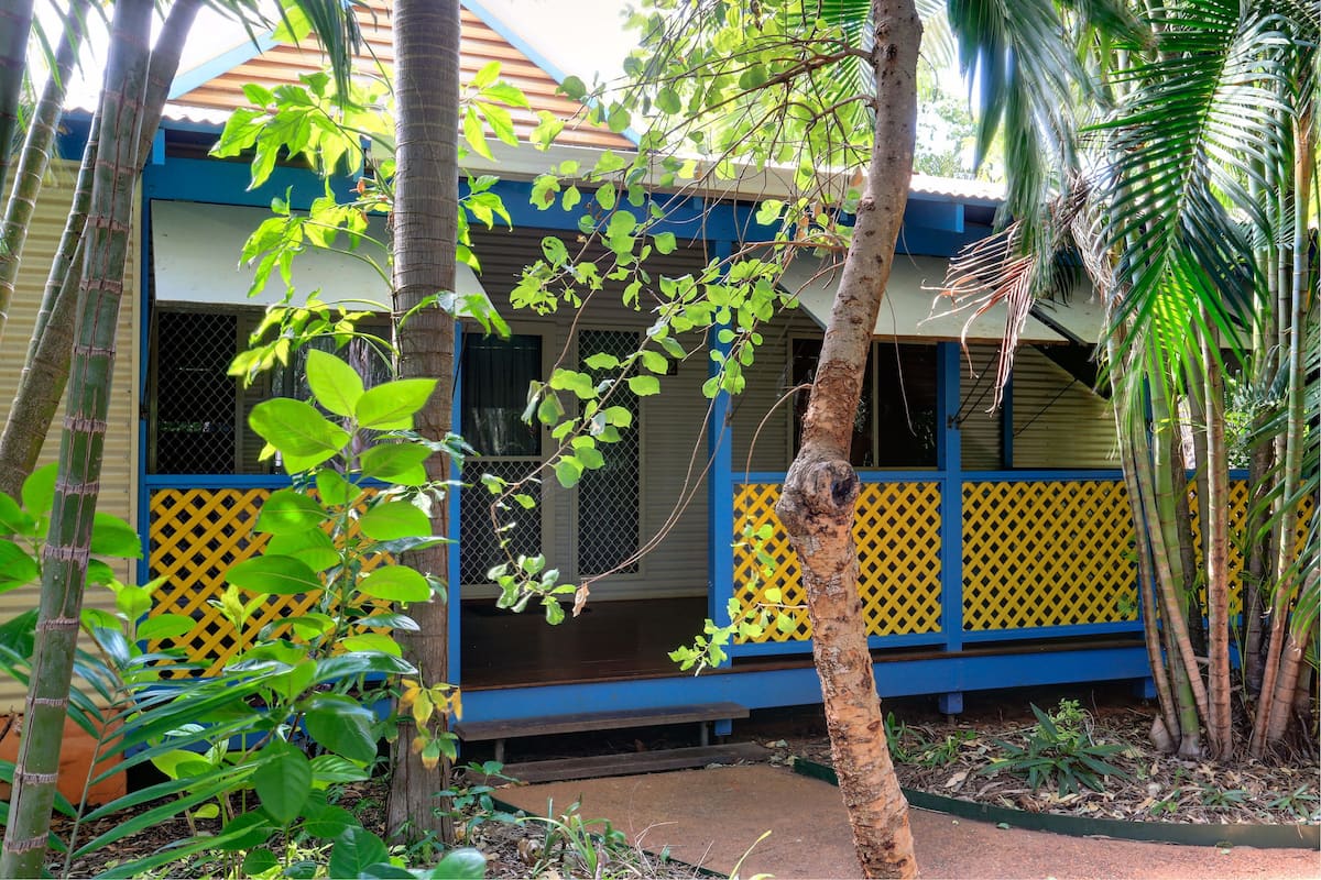 A house with a blue and yellow exterior, surrounded by lush greenery and trees.