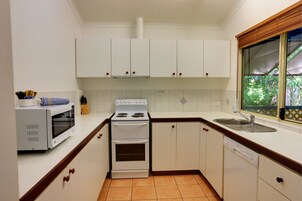Una cocina con gabinetes blancos, estufa, microondas y lavavajillas.