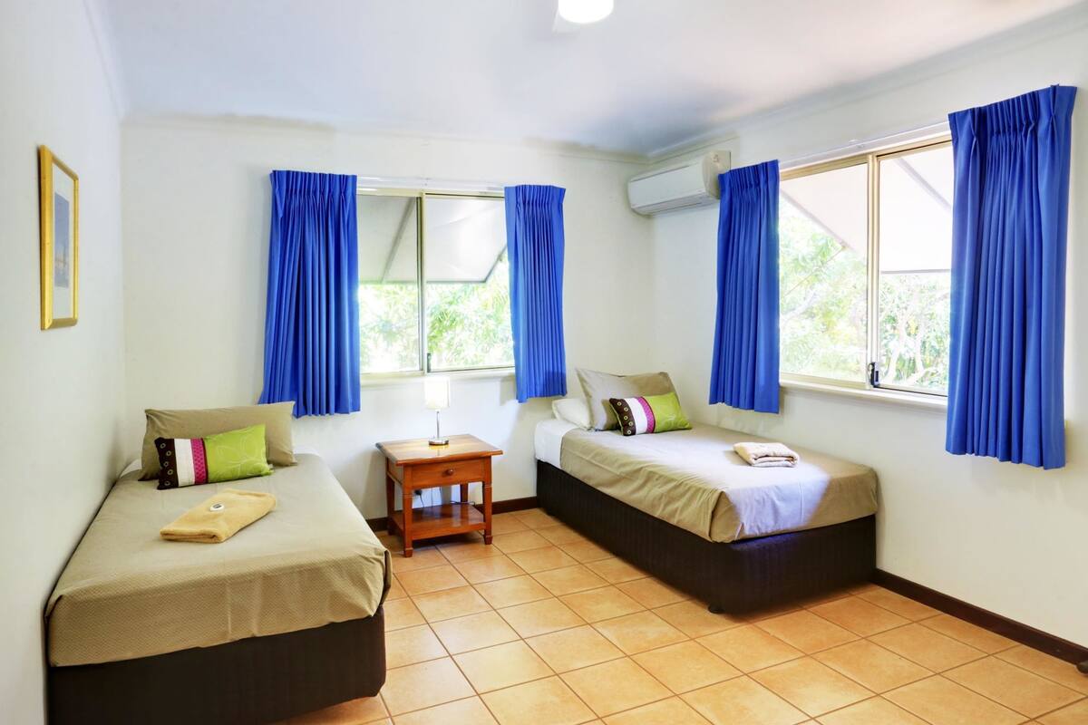 A room with two beds, a small table, and a window with curtains.