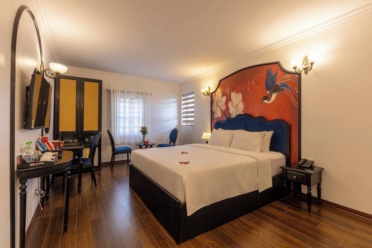 Une chambre d’hôtel avec un grand lit, un bureau avec une chaise, une petite table avec une lampe et un tableau au mur.