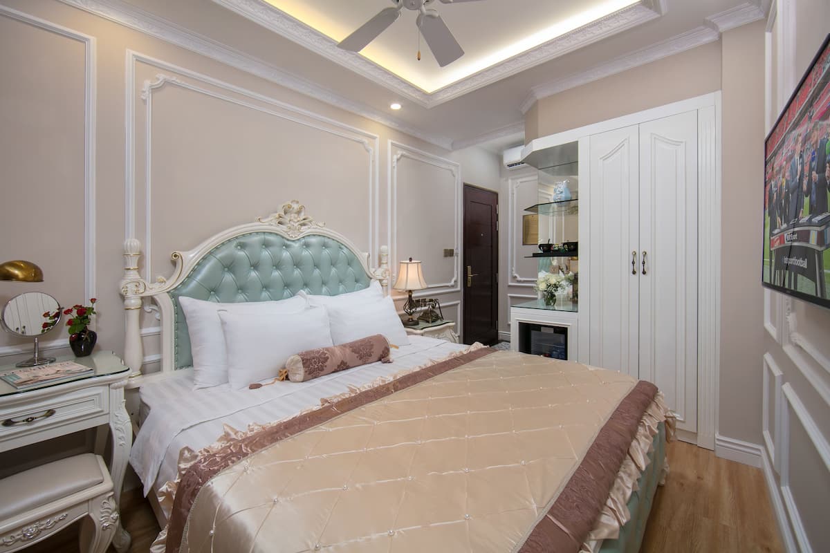A bedroom with a large bed, a nightstand with a lamp, a dresser, and a wardrobe.