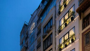 Un hôtel à étages, doté de balcons ornés de plantes en pot et d’une façade bien éclairée.