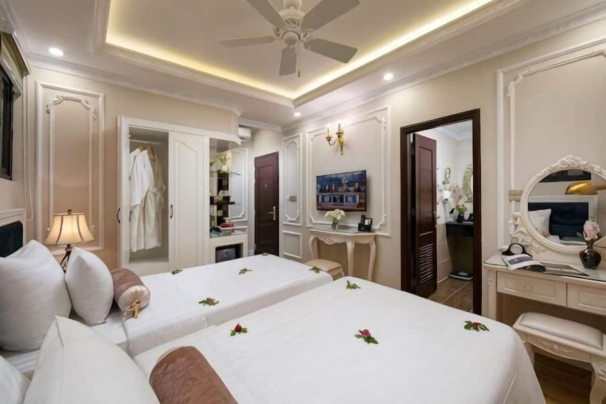 A hotel room with two beds, a vanity with a mirror, a desk, and a ceiling fan.