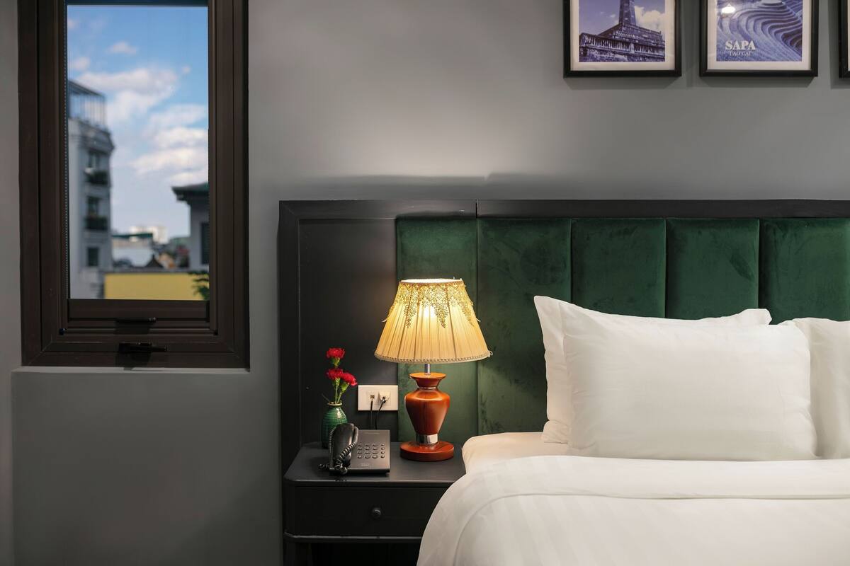 A hotel room with a bed, a nightstand with a lamp, a vase with flowers, and framed pictures on the wall.