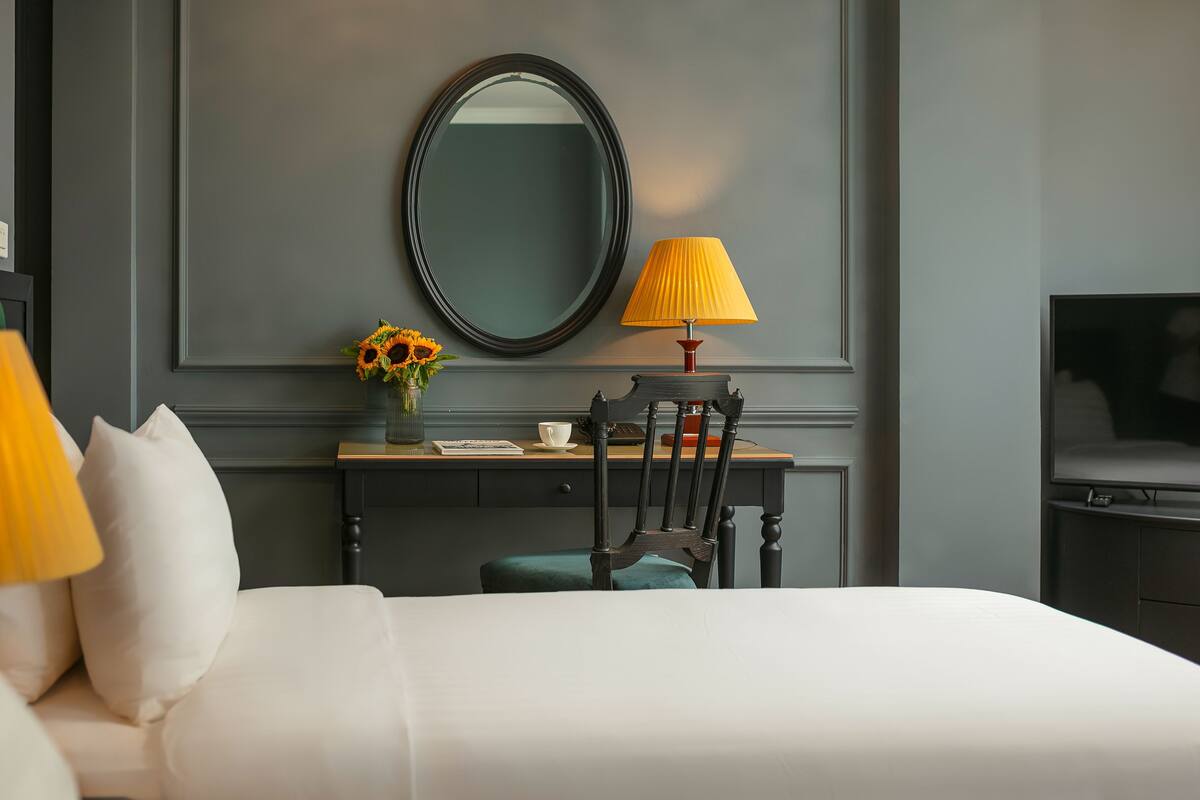 A hotel room with a bed, a desk with a lamp, a chair, a mirror, and a television.