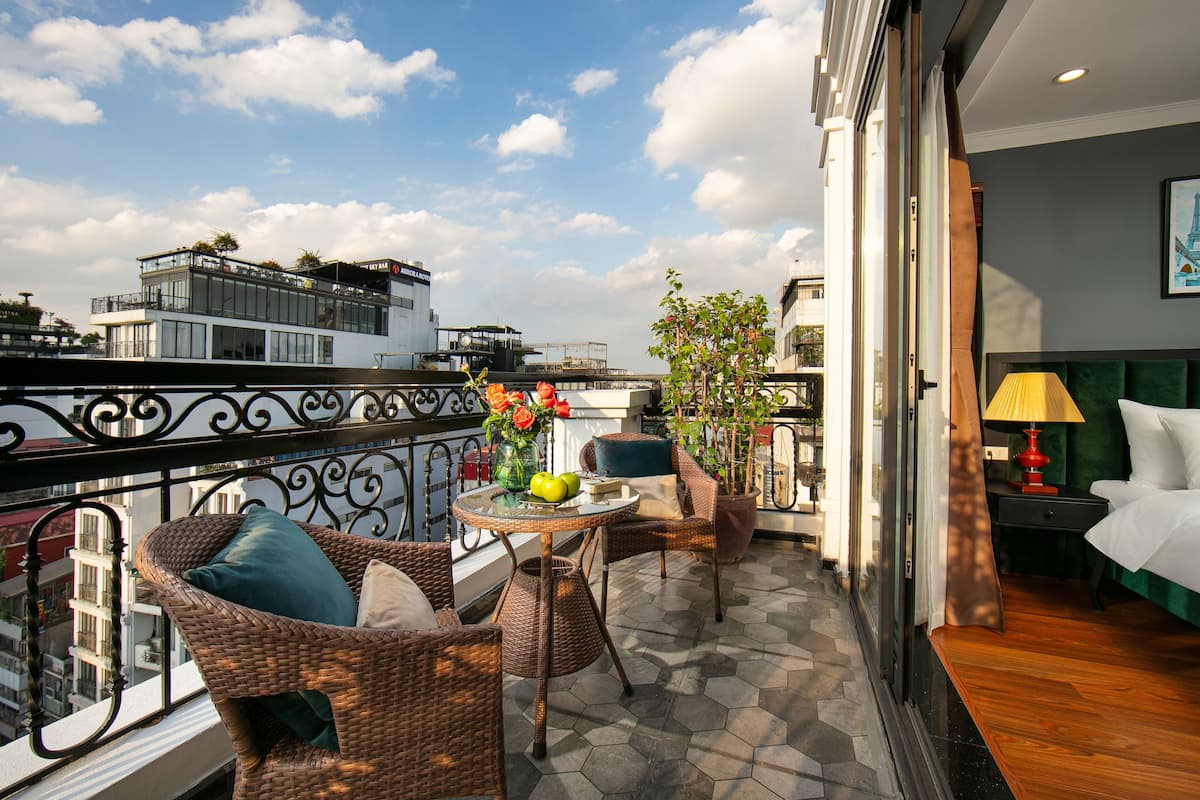 A balcony with wicker furniture, a table with fruit and flowers, and a view of the cityscape.