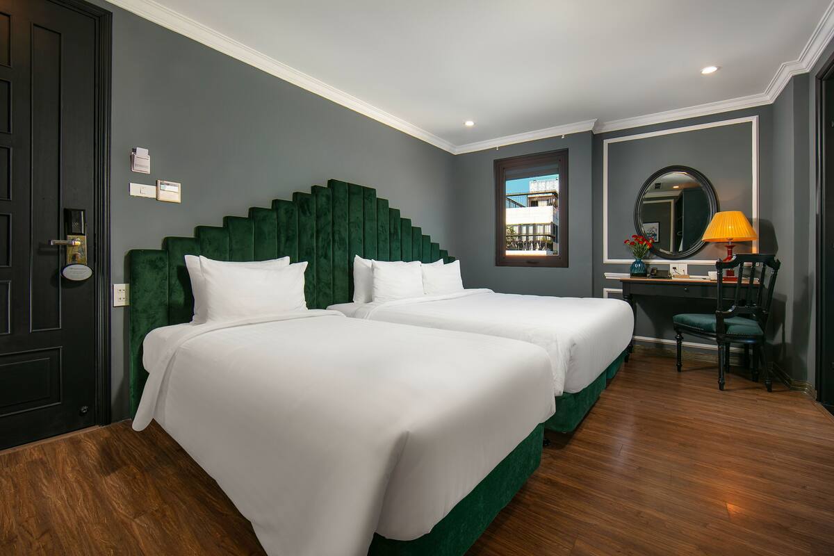 A hotel room with two beds, a desk, a chair, a mirror, and a window.
