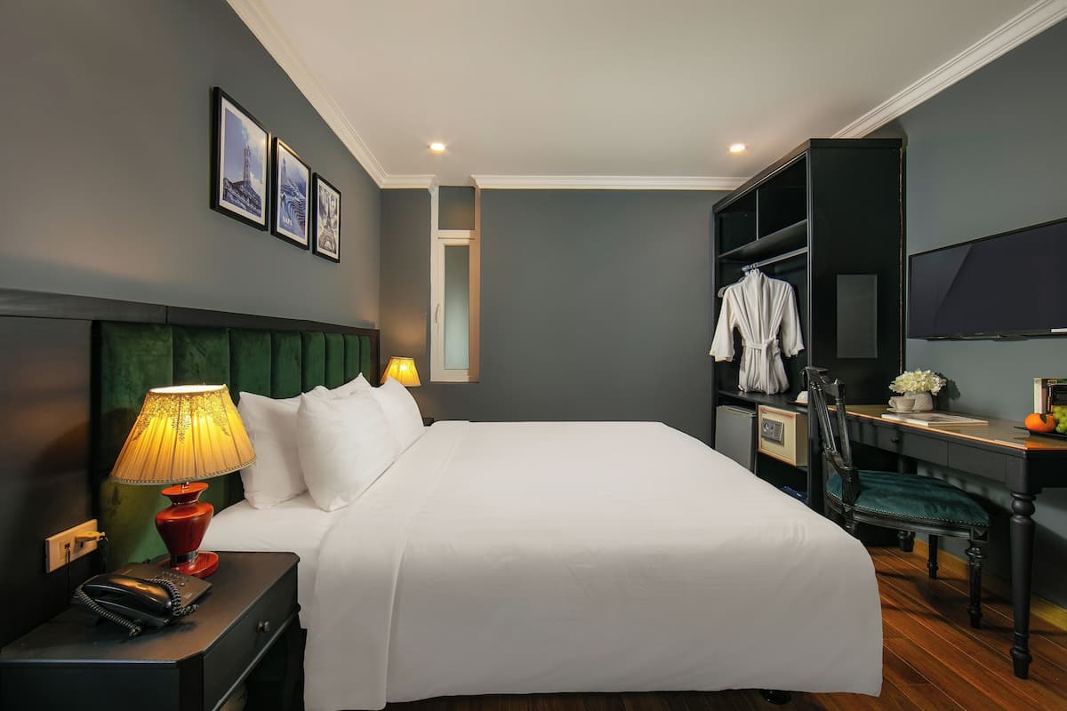 A hotel room with a bed, a desk with a chair, a TV, and a wardrobe.